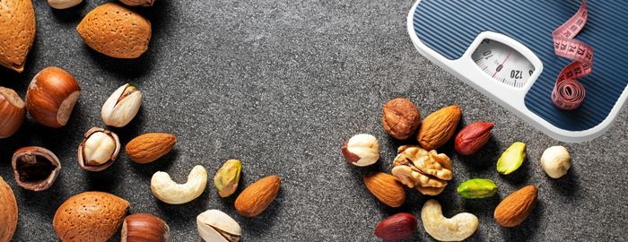 Visual of mixed nuts, a weighing scale and measuring tape. Are nuts good for weight loss.